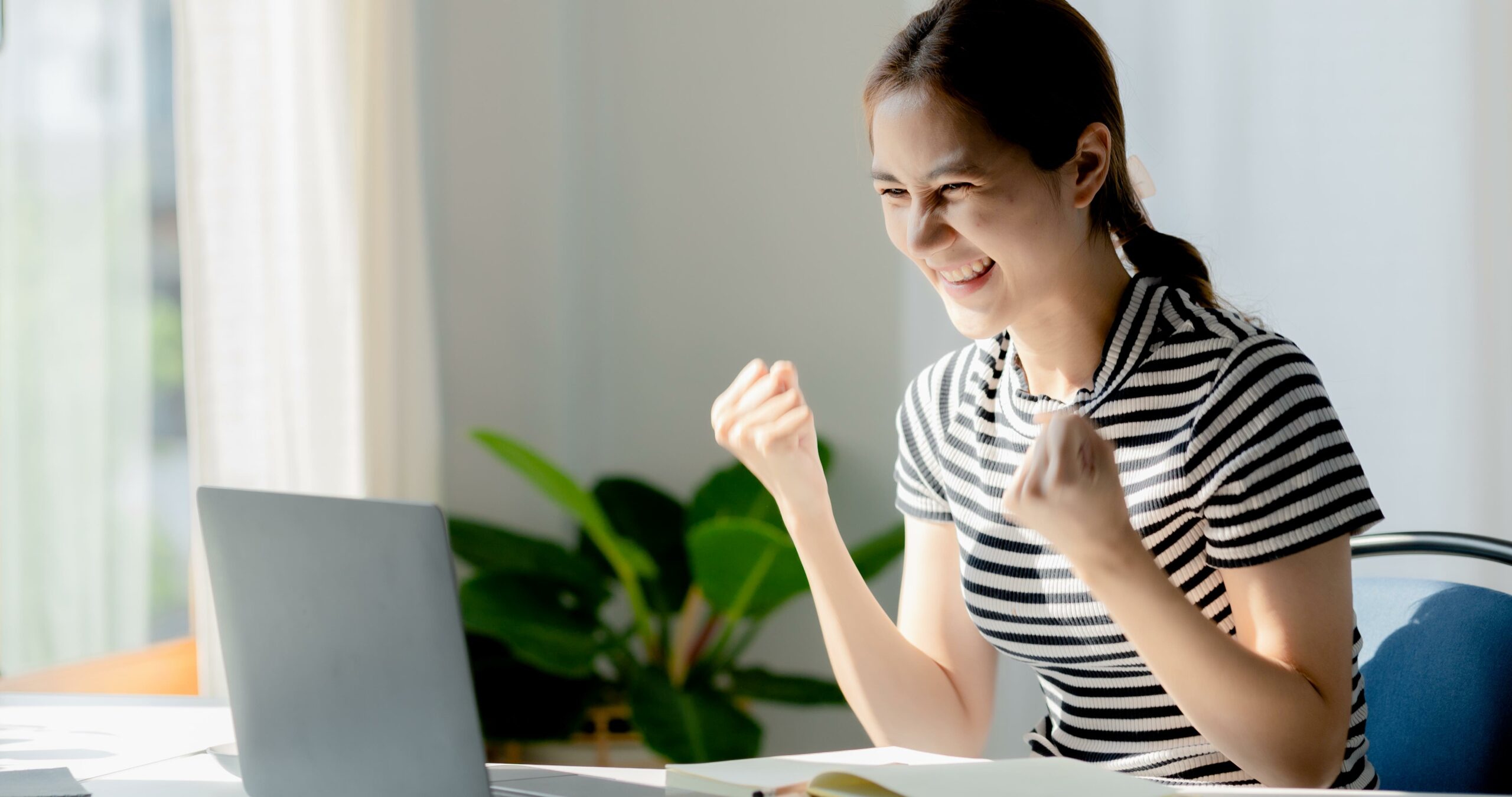 An Asian woman looks delighted after checking her exam results, she is a university student, The concept of online learning due to the COVID-19 outbreak to prevent an outbreak in the classroom.