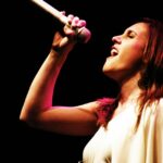 Una Mujer Cantando Con Un Micrófono En La Mano.